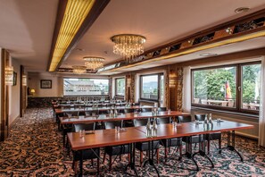 A conference room with multiple tables and chairs, large windows with a view of greenery, and ornate chandeliers. - Sauerland Alpin Hotel (Schmallenberg)
