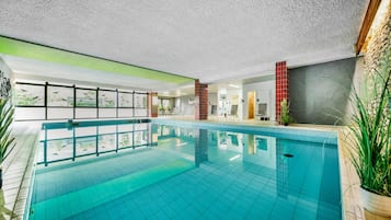 An indoor swimming pool with clear glass walls, a tiled floor, and a ceiling with a textured finish.