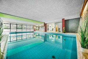 An indoor swimming pool with clear glass walls, a tiled floor, and a ceiling with a textured finish. - Sauerland Alpin Hotel (Schmallenberg)