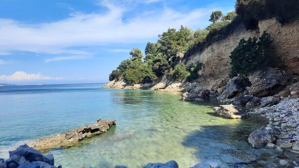 A coastal landscape with clear water, rocky shore, and dense vegetation on a hillside. - Casa Spiaggia (Zakynthos - Limni Keriou)