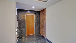 A modern elevator with a wooden door and a control panel, surrounded by polished granite walls and a metal handrail.