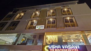 A hotel with multiple floors, large windows with yellow railings, and a sign for 'USHA VASAVI THE BOUTIQUE HOTEL'.