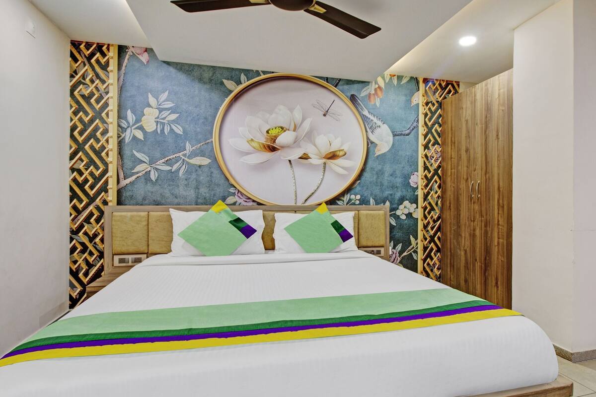 A bedroom with a bed, a ceiling fan, a wall with floral wallpaper, and a wooden wardrobe.