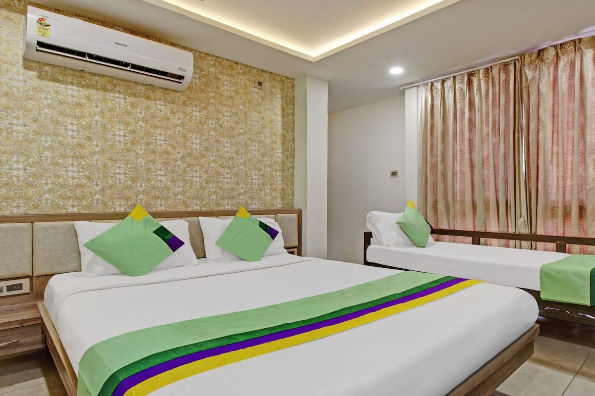 A hotel room with a large bed, a smaller bed, an air conditioning unit, a nightstand, and a window with curtains.