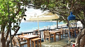 An outdoor dining area with wooden tables and chairs, overlooking a beach. - Melinda Pansiyon (Datça)