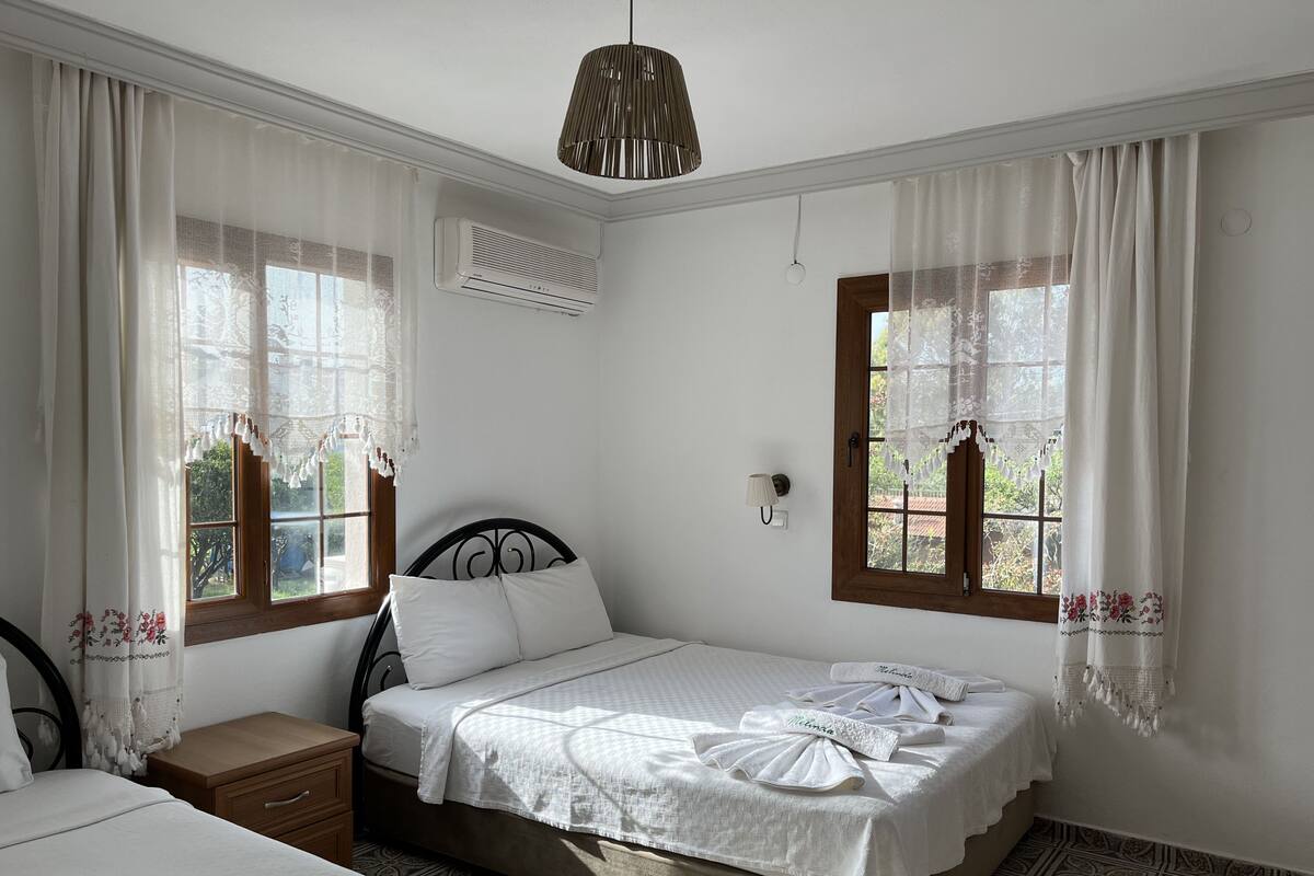 A bedroom with a bed, a nightstand, a wall-mounted lamp, and a window with curtains.