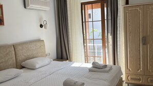 A hotel room with a bed, a wardrobe, a window with curtains, and an air conditioning unit.