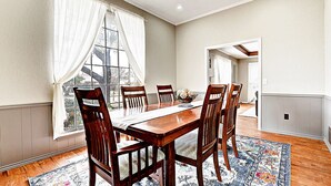 Comedor con mesa y sillas de madera, un ventanal con cortinas y vistas al exterior.