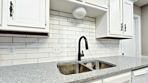Una cocina con armarios blancos, encimera de granito y pileta de acero inoxidable.