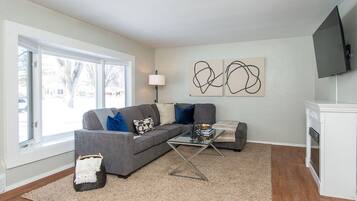A modern living room with a grey sectional sofa, a glass coffee table, and abstract wall art.