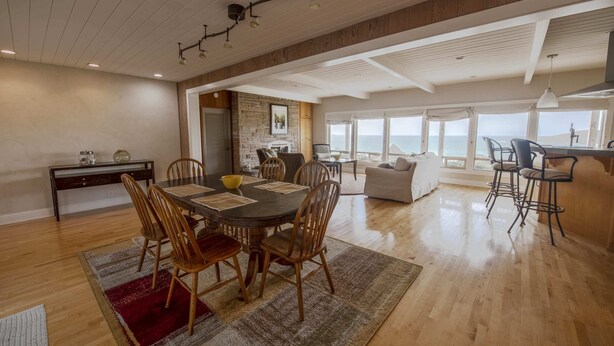 A spacious dining area with a wooden table and chairs, a kitchen area with a stone backsplash, and a view of the ocean through large windows. - Spectacular Ocean Front Views "Sea Star Escape" A (Brookings)