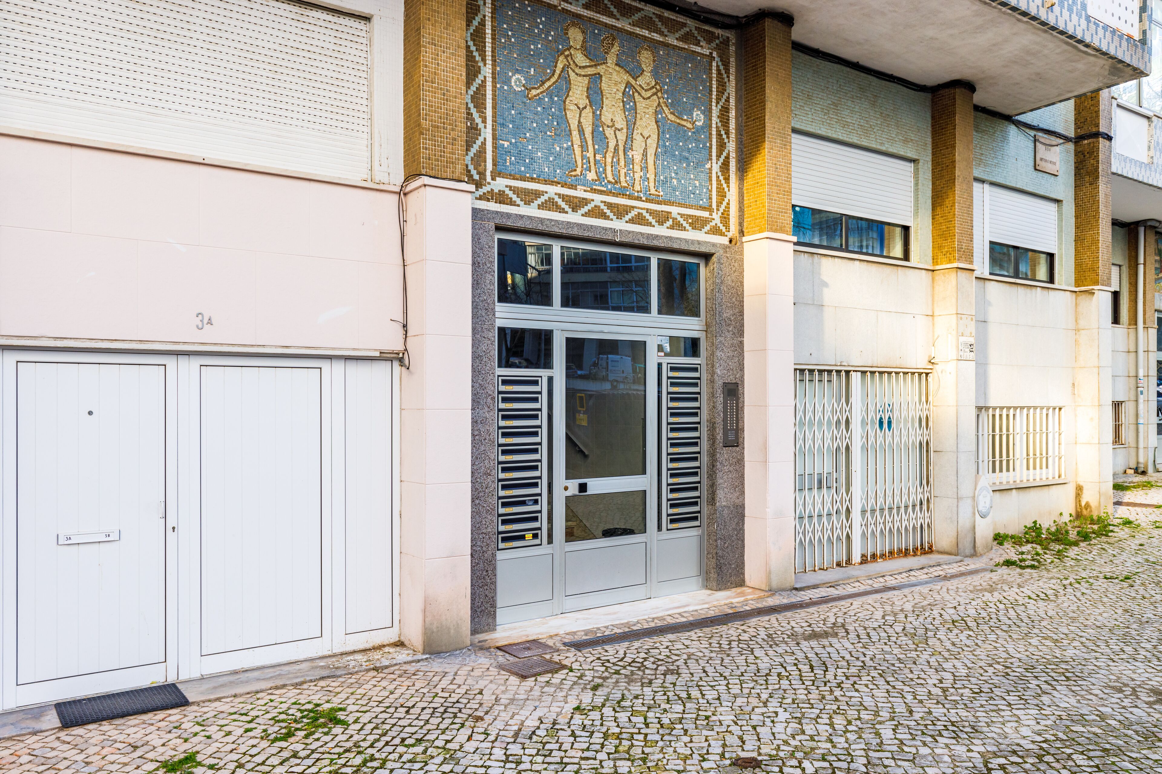 A building facade with a mosaic, a set of double doors, and a cobblestone street.