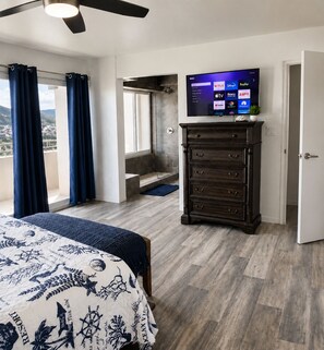 Een hotelkamer met een bed, een dressoir, een televisietoestel dat verschillende zenders toont en een balkon met gordijnen.