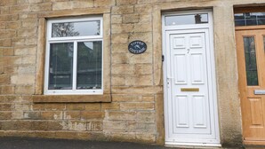 A stone building with a white door and a window. There is a sign on the wall that reads "Yippee Cottage." - Yippee Cottage (Keighley)