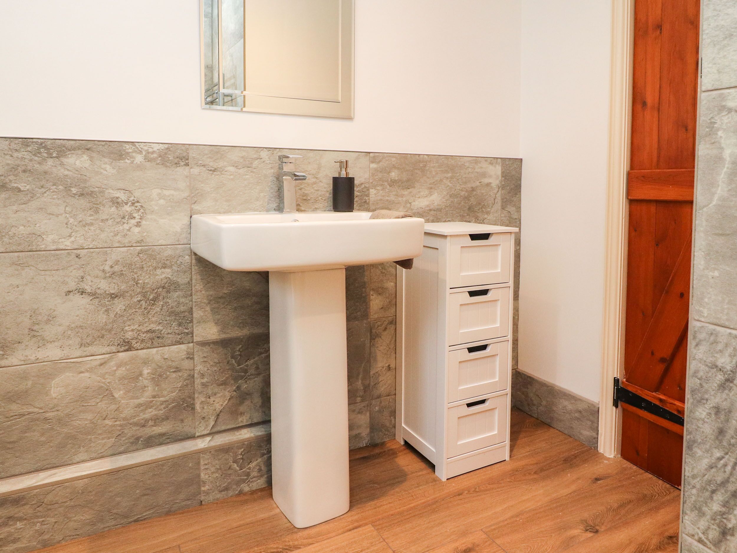A bathroom with a white pedestal sink, a mirror above it, and a wooden door.