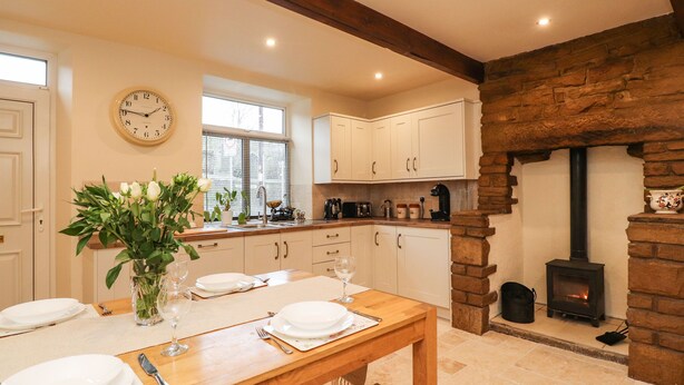 A cozy kitchen with white cabinets, a stone fireplace, and a dining table set for four. - Yippee Cottage (Keighley)