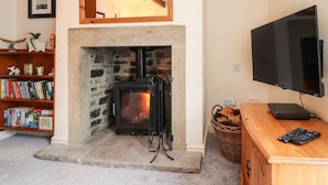 A cozy living room with a stone fireplace, a television, and a bookshelf filled with books. - Yippee Cottage (Keighley)