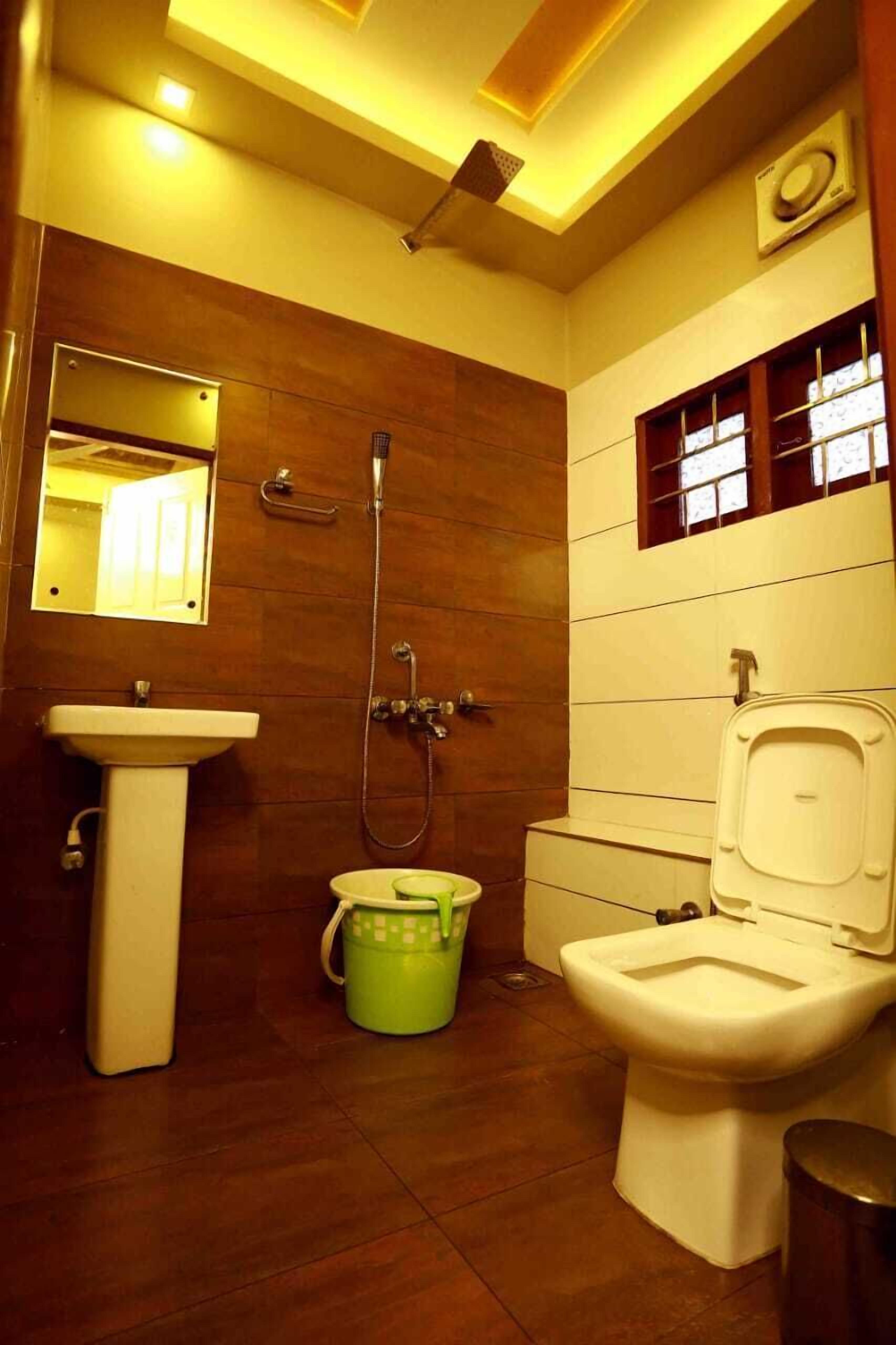 A bathroom with a sink, toilet, shower, and a green bucket.