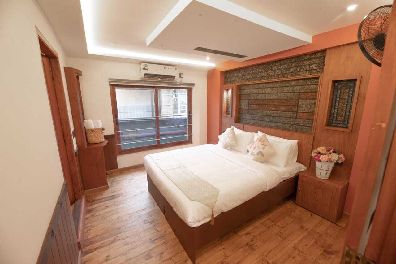 A bedroom with a large bed, wooden flooring, a window with blinds, and a wall-mounted air conditioner.