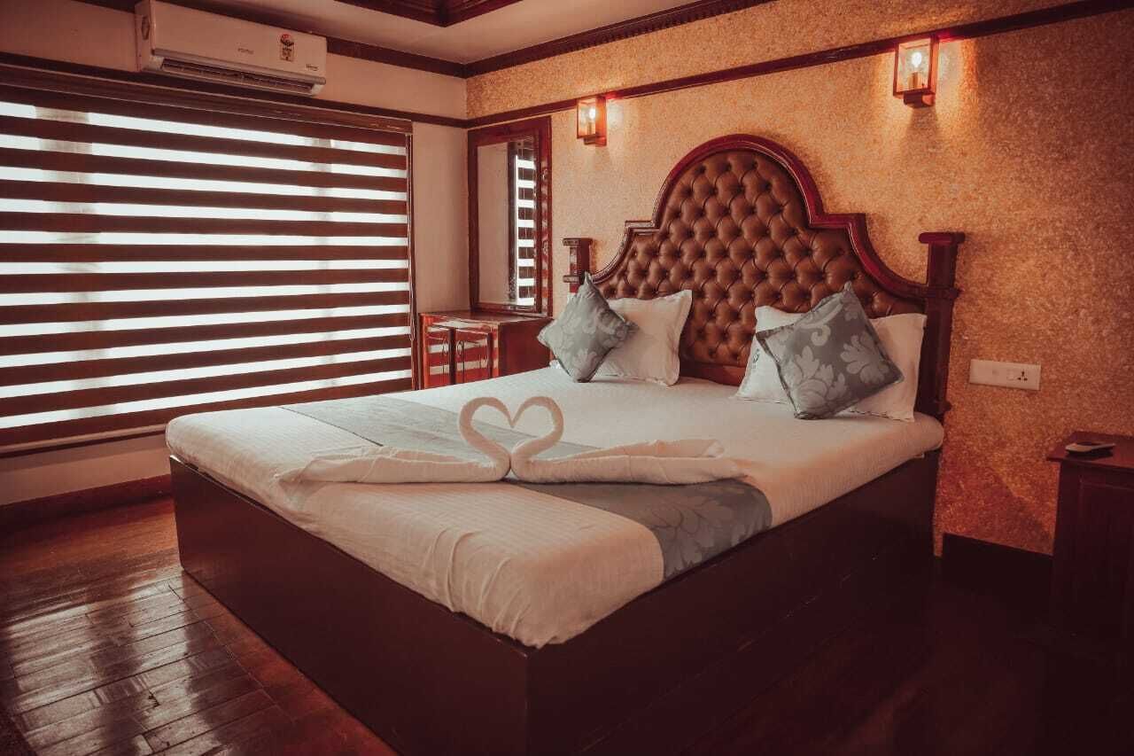 A large bed with a heart-shaped towel arrangement, a wooden headboard, and a small table beside the window.