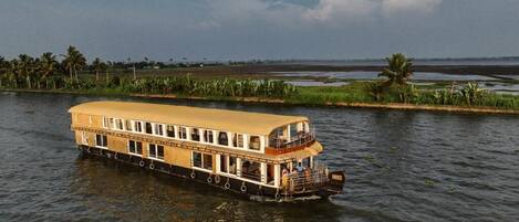A riverboat with a flat deck and multiple windows, floating on calm water.