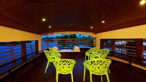 An indoor seating area with a view of the water, featuring bright yellow chairs and a wooden ceiling. - Double Decker Houseboat (Ambalapuzha)
