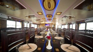 A train dining car with tables set for dining, a central aisle, and a large screen at the front. - Double Decker Houseboat (Ambalapuzha)