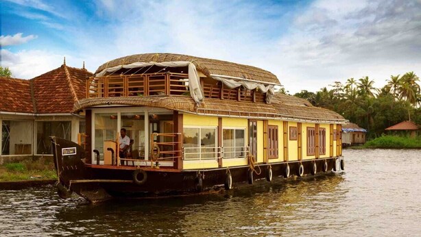 A houseboat with a thatched roof, wooden deck, and windows. - Double Decker Houseboat (Ambalapuzha)