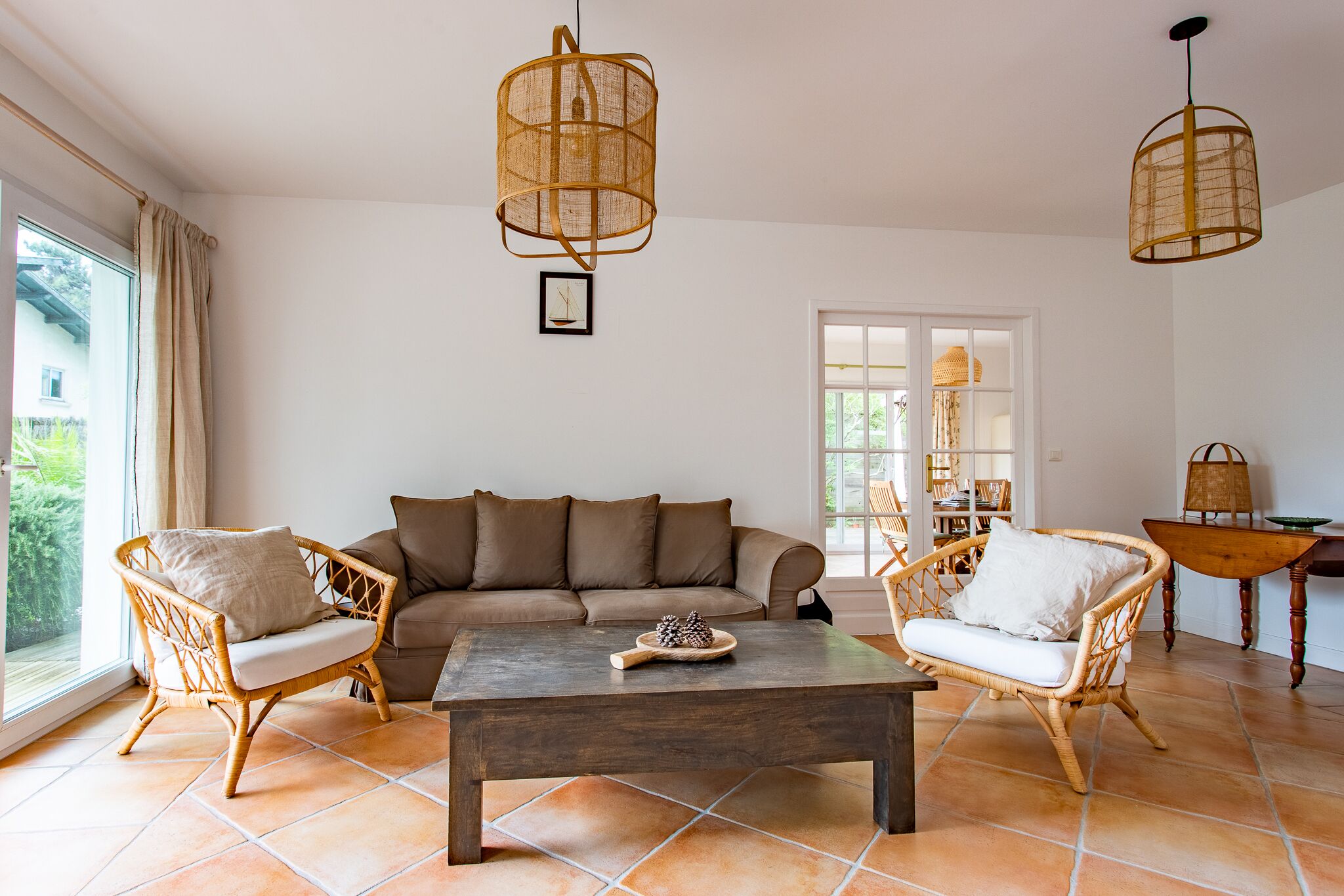 Ein Wohnzimmer mit einer Couch, zwei Korbstühlen, einem Couchtisch und zwei hängenden Lampen aus Korb.