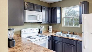 Una cocina con armarios oscuros, un horno blanco, un microondas y un lavabo.