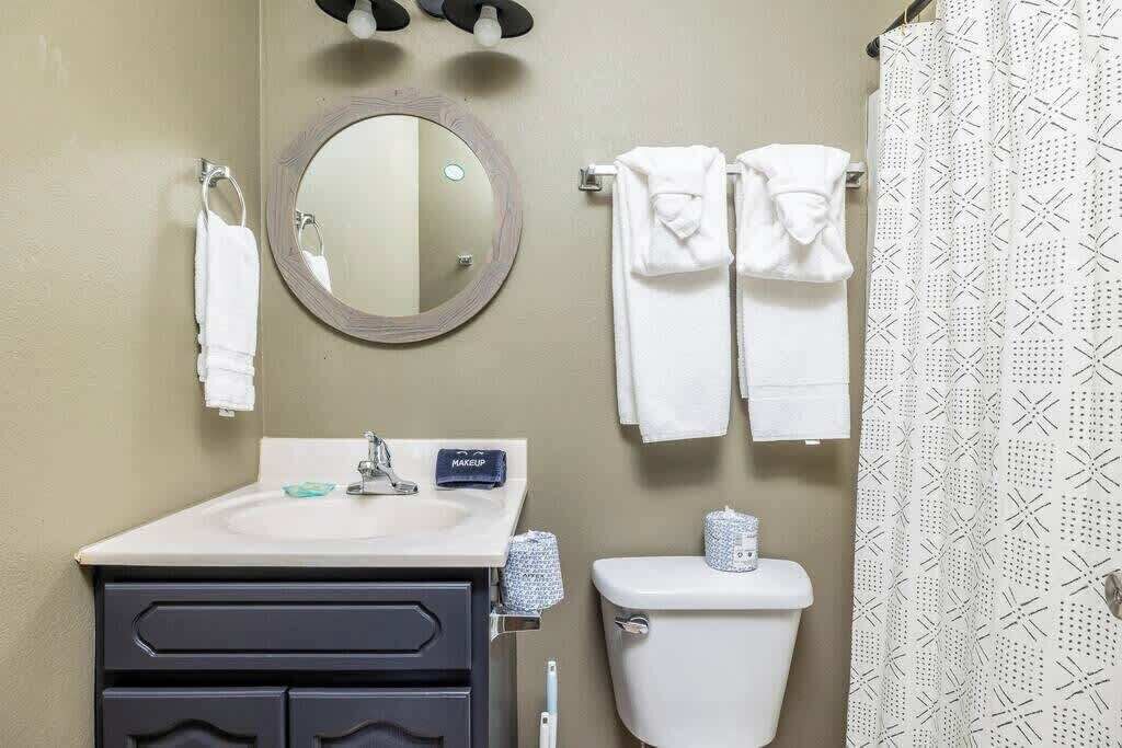 A bathroom with a round mirror, a sink, a toilet, and two towels hanging on a rack.