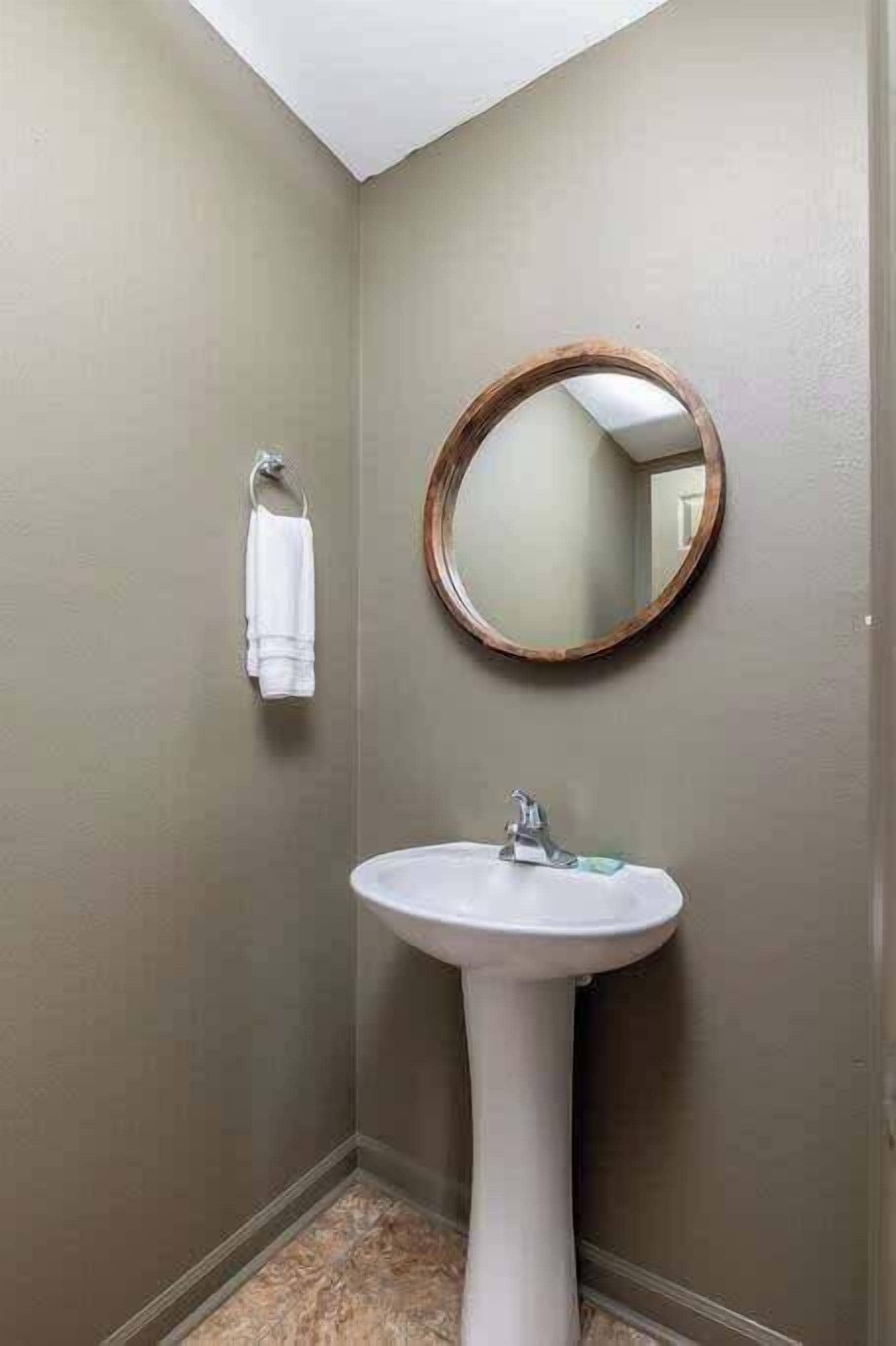 A small bathroom with a white pedestal sink, a round mirror, and a towel hanging on the wall.