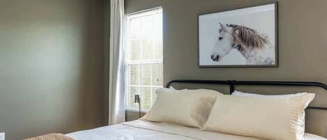 Ein Schlafzimmer mit einem Bett, Kissen, einer Decke, einem Fenster und einem Wandbild eines Pferdes.