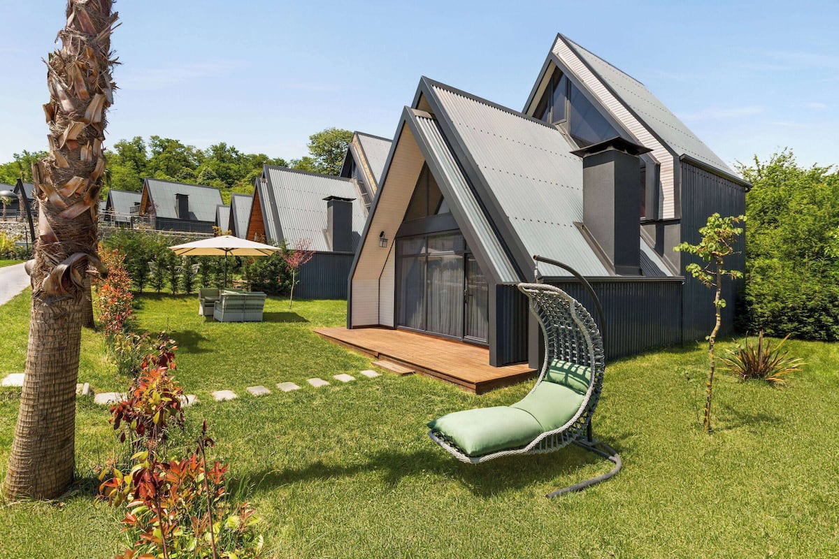 A modern house with a sloped roof, a patio with a swing chair, and a well-maintained lawn.