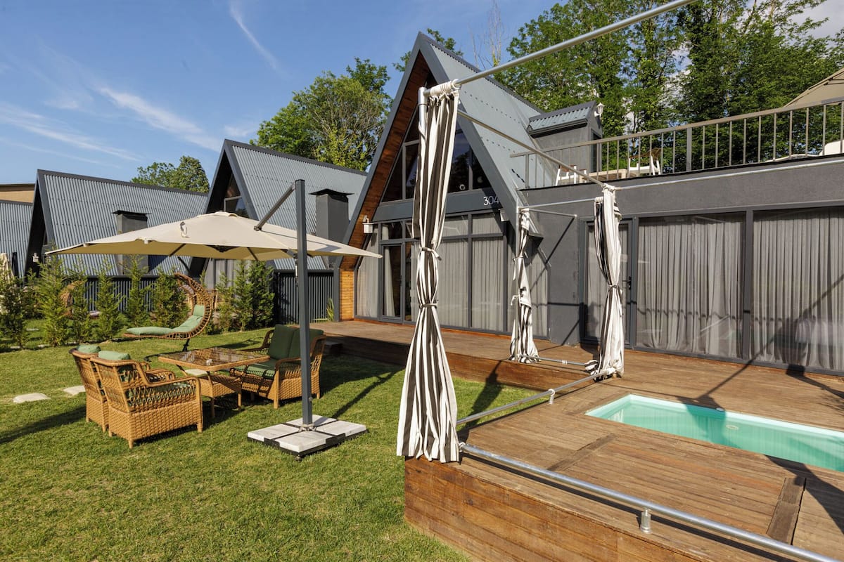 A modern outdoor pool area with a wooden deck, lounge chairs, and umbrellas.