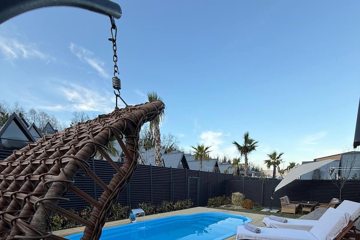 A wooden deck with a pool, lounge chairs, and a hanging chair.