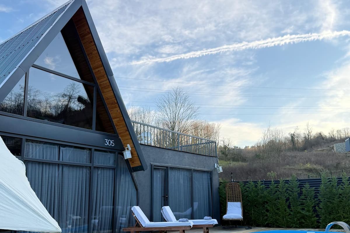 A modern building with a sloped roof, a swimming pool, and two lounge chairs.
