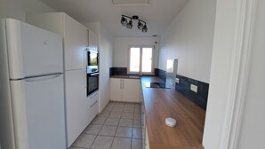 A modern kitchen with white cabinetry, a built-in oven, and a wooden countertop. - Maison Bord de mer Avec Jardin Clos (Ploudalmézeau)