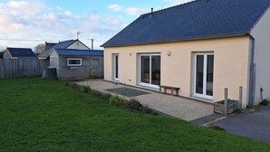 A single-story house with a dark roof, a front porch, and a sliding glass door. - Maison Bord de mer Avec Jardin Clos (Ploudalmézeau)