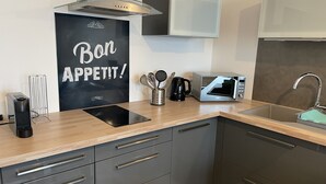 A modern kitchen with a black countertop, stainless steel appliances, and a backsplash with the text "Bon APPETIT!". - Petit Cocon Courseullais with 2-star sea view (Courseulles-sur-Mer)