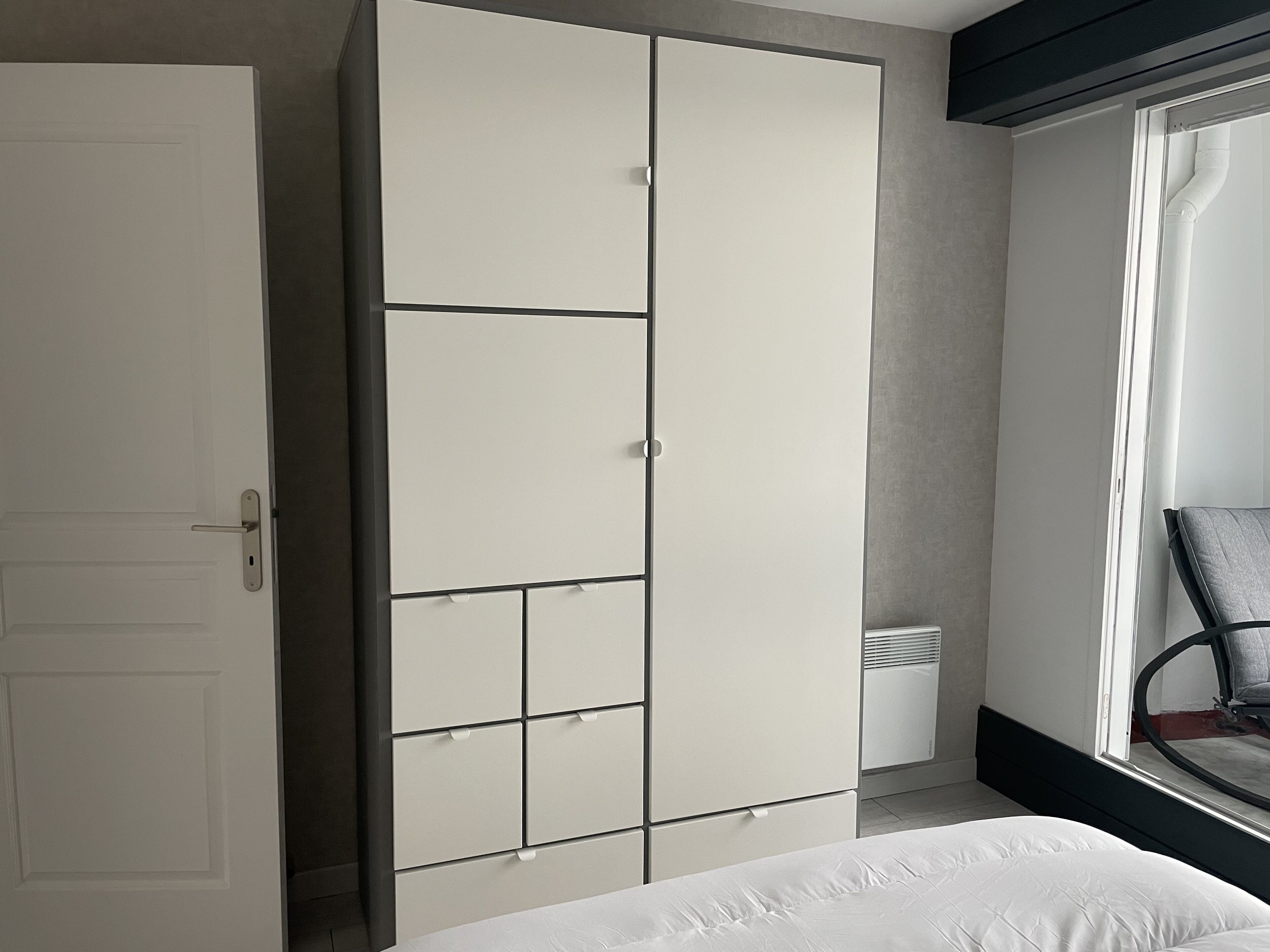 A bedroom with a large wardrobe, a bed, and a window with blinds.