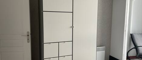 A bedroom with a large wardrobe, a bed, and a window with blinds.