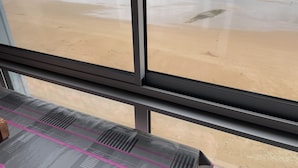 A view of a beach through a window, with a sandy shore and ocean waves visible. - Petit Cocon Courseullais with 2-star sea view (Courseulles-sur-Mer)