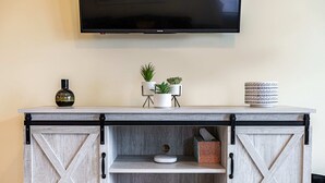 A wooden cabinet with a TV mounted above it, two potted plants, and a decorative item on the top shelf. - Large 4BR Stadium Getaway, Walk to the Big House! (Ann Arbor)