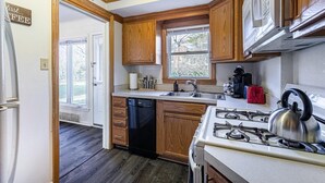 A compact kitchen with wooden cabinets, a dishwasher, a stove, and a window providing natural light. - Large 4BR Stadium Getaway, Walk to the Big House! (Ann Arbor)