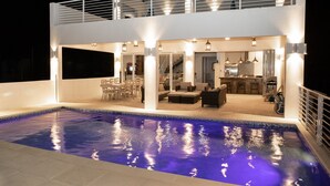 Una casa de dos pisos con piscina, mobiliario exterior y zona de cocina.