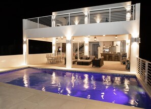 Una casa de dos pisos con piscina, mobiliario exterior y zona de cocina.