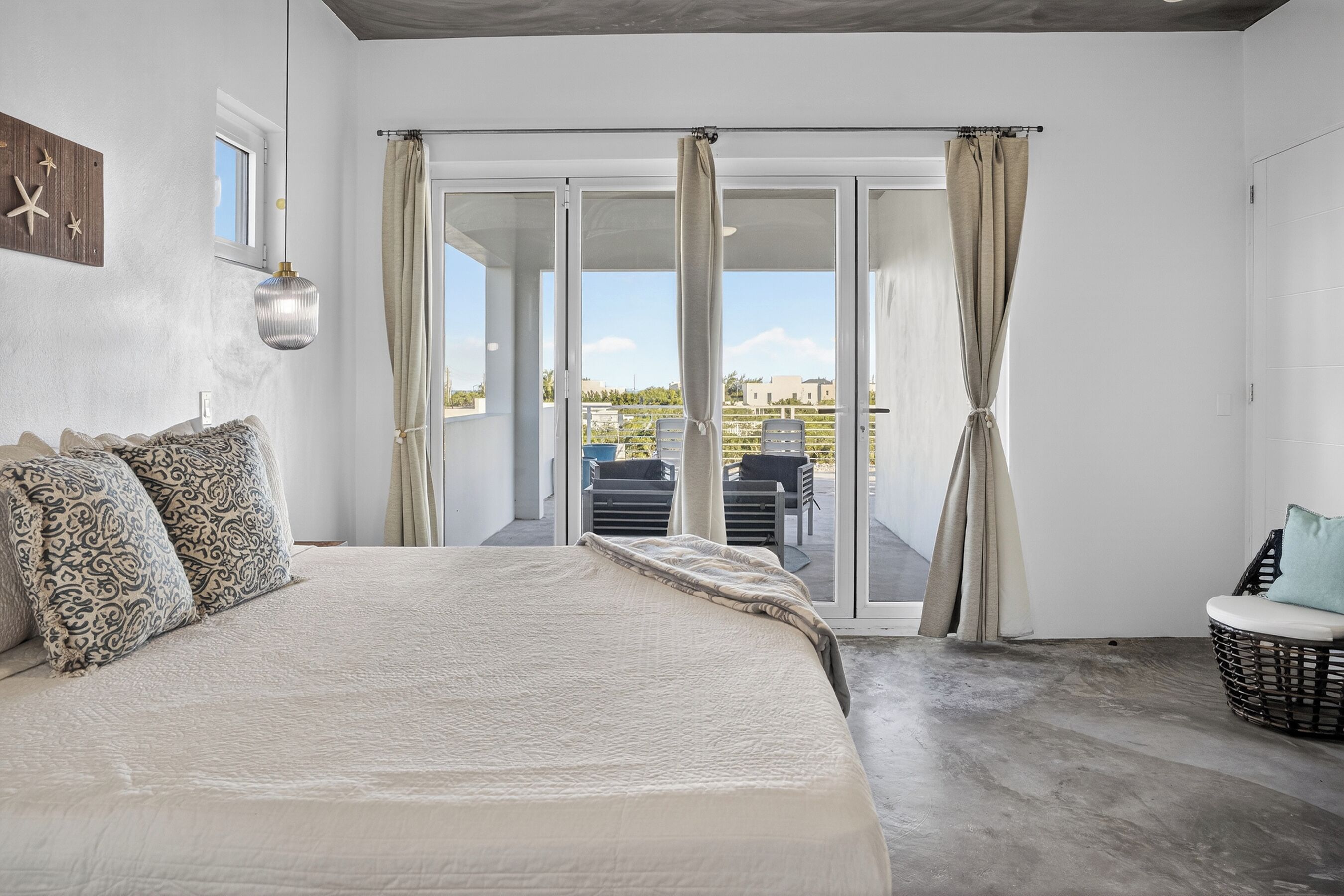 A bedroom with a large bed, a balcony with a view, and a wicker chair.