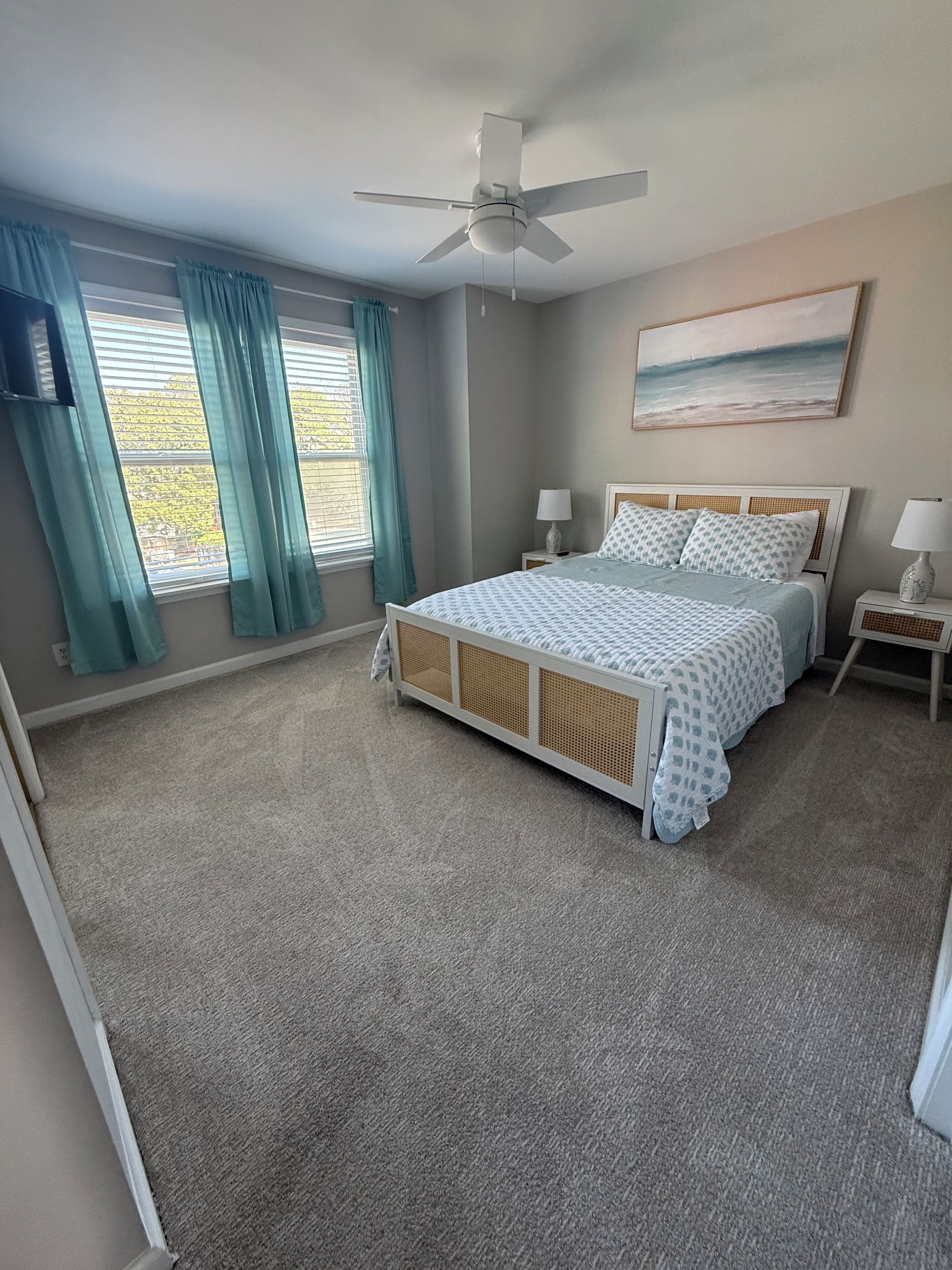 A bedroom with a bed, a ceiling fan, a nightstand, a lamp, and a painting on the wall.