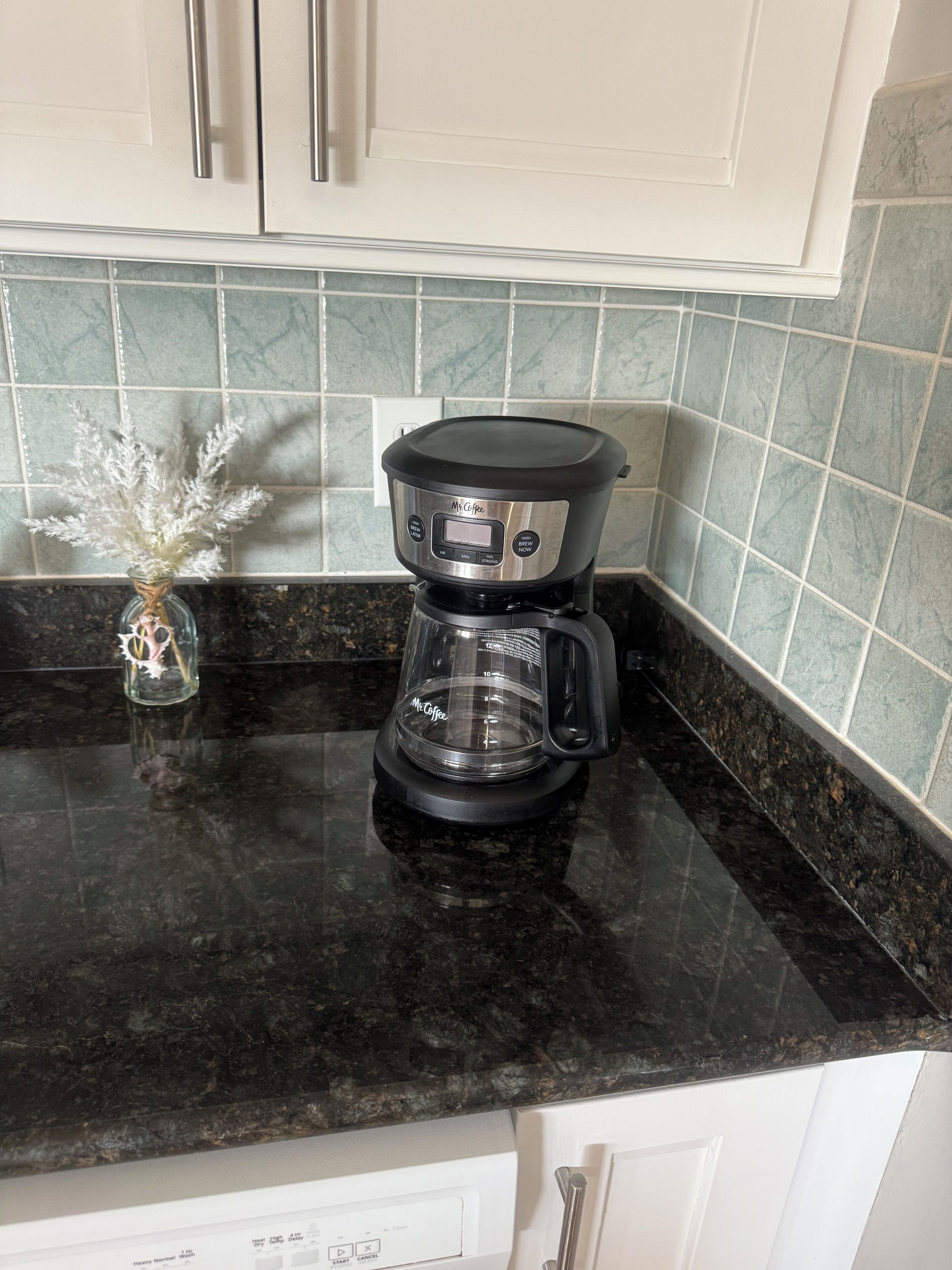 Eine Kaffeemaschine auf einer Küchenarbeitsplatte mit einer Vase getrockneter Blumen.